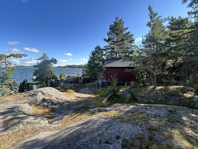 Capanna sauna rossa in legno sulla riva di un lago tra i pini, in Svezia