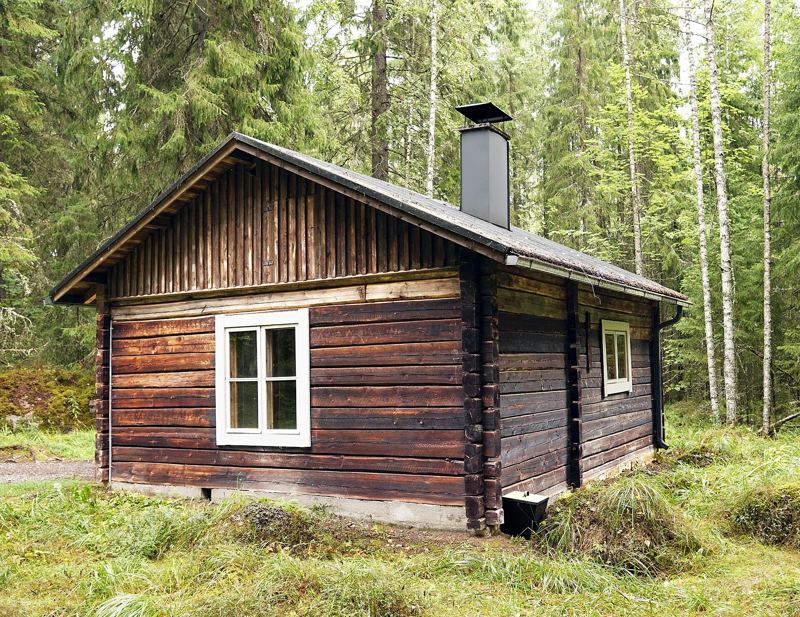 Traditional dark wooden sauna cabin with chimney in a forest