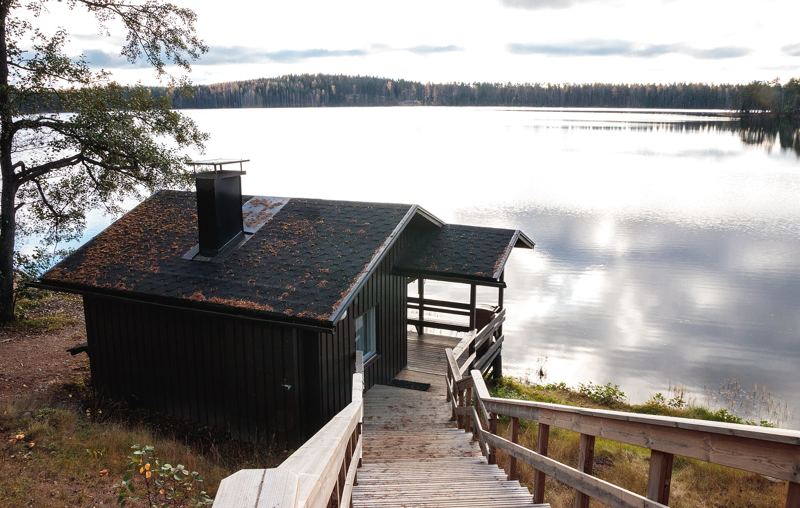 Wooden sauna hut with chimney and jetty by the lake